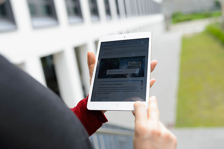 Eine Person hält ein Tablet in der Hand. Dort ist die Website von PUBLISSO aufgerufen.